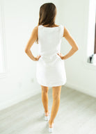 Woman wearing a white dress standing in a minimalistic room.