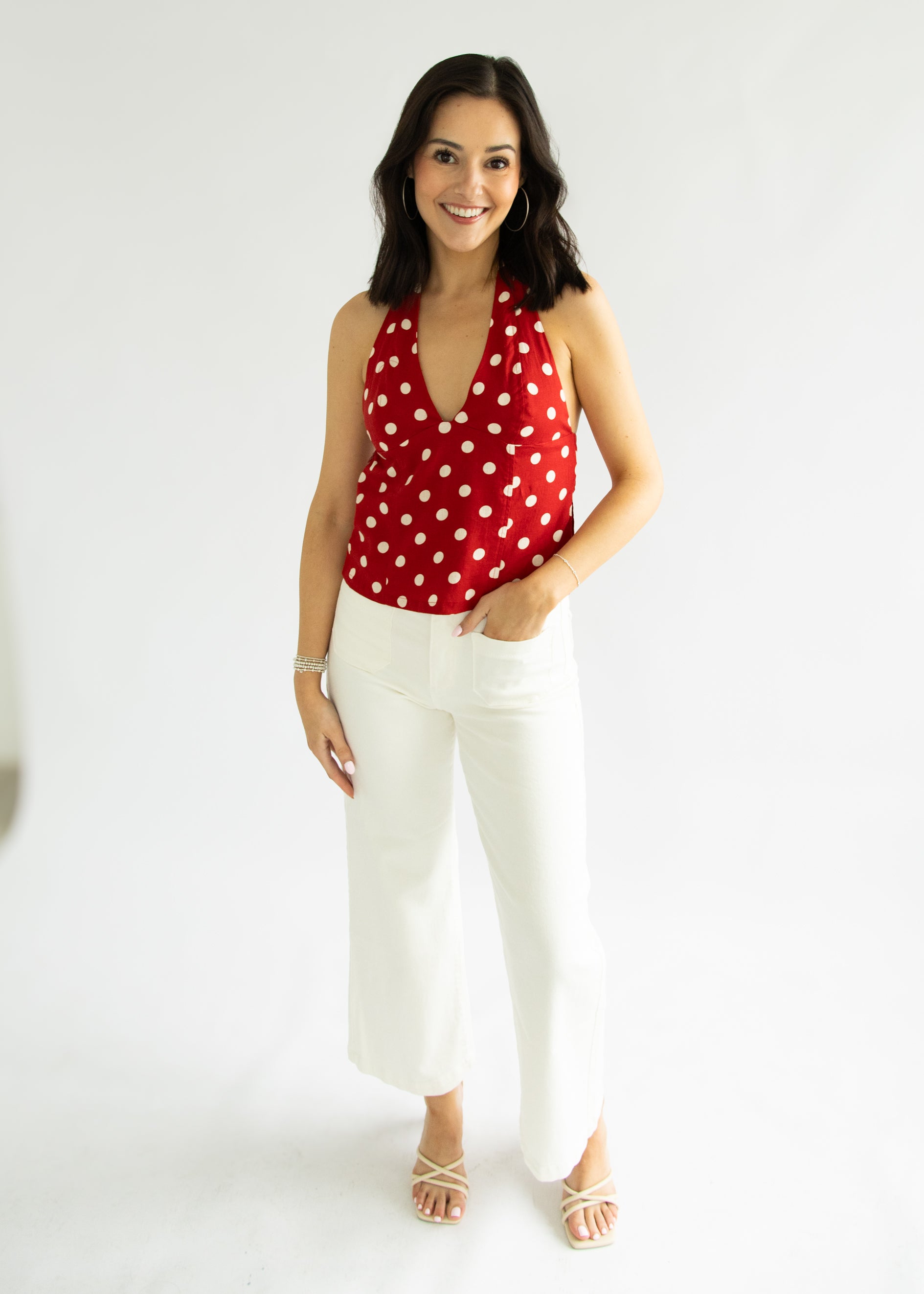 Woman wearing a red polka dot top and white pants on a white background