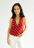 Woman wearing a red polka dot top and white pants on a plain background