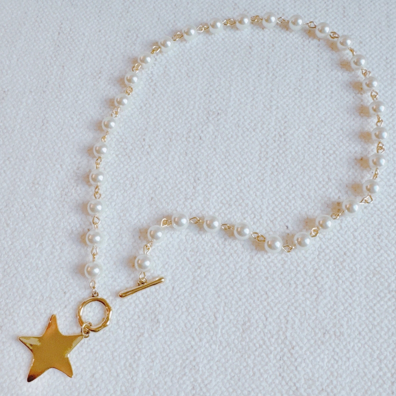 Pearl necklace with a gold star charm on a light gray background