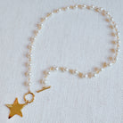 Pearl necklace with a gold star charm on a light gray background