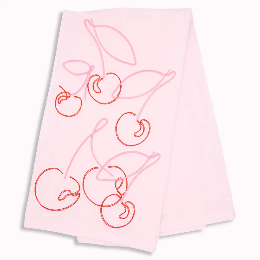 A light pink fabric napkin or tea towel featuring a minimalist line-art design of cherries with stems in shades of pink and red, shown against a plain white background.