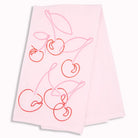 A light pink fabric napkin or tea towel featuring a minimalist line-art design of cherries with stems in shades of pink and red, shown against a plain white background.