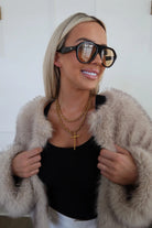 Woman wearing a fur coat, black top, and sunglasses with a white background