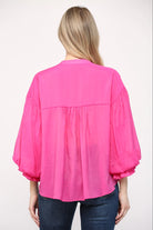 Person wearing a bright pink blouse with long sleeves on a white background