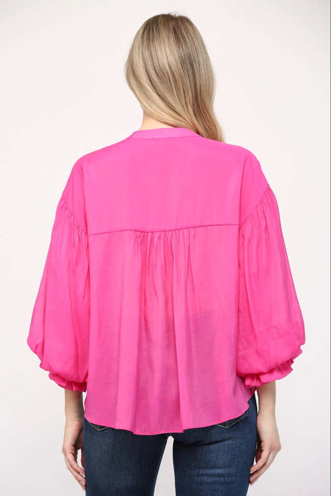 Person wearing a bright pink blouse with long sleeves on a white background