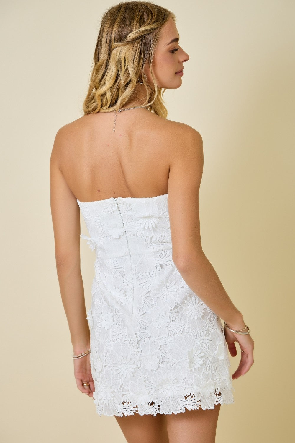 Woman wearing a white lace strapless dress against a beige background