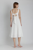Woman wearing a white dress with cut-out back design on a plain background