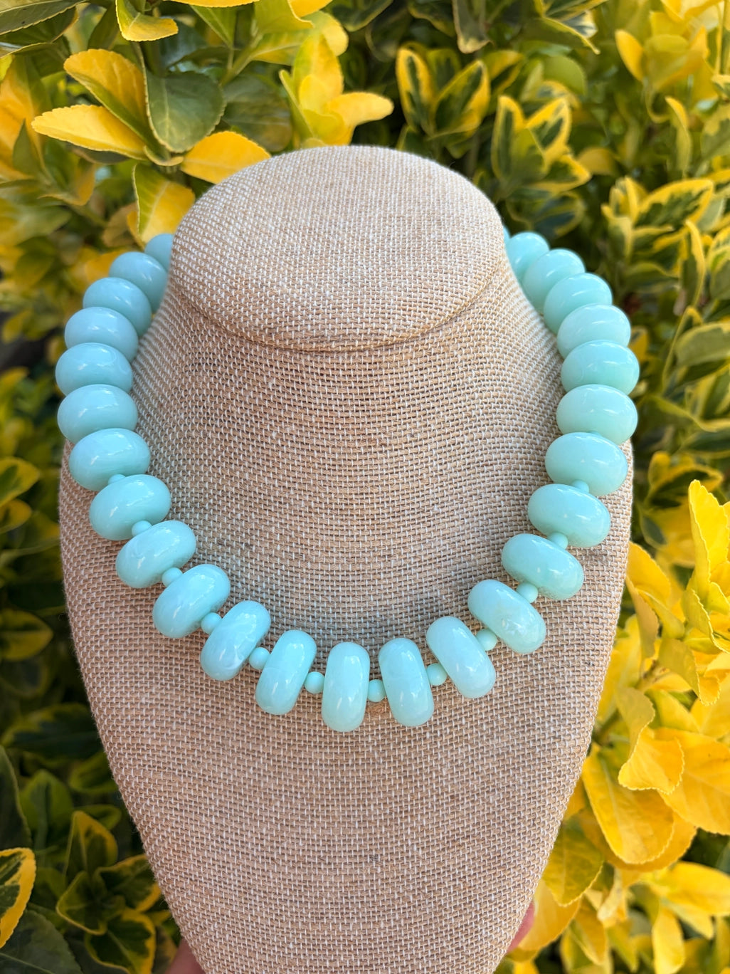 Turquoise mint beaded necklace on a bust with green foliage in the background