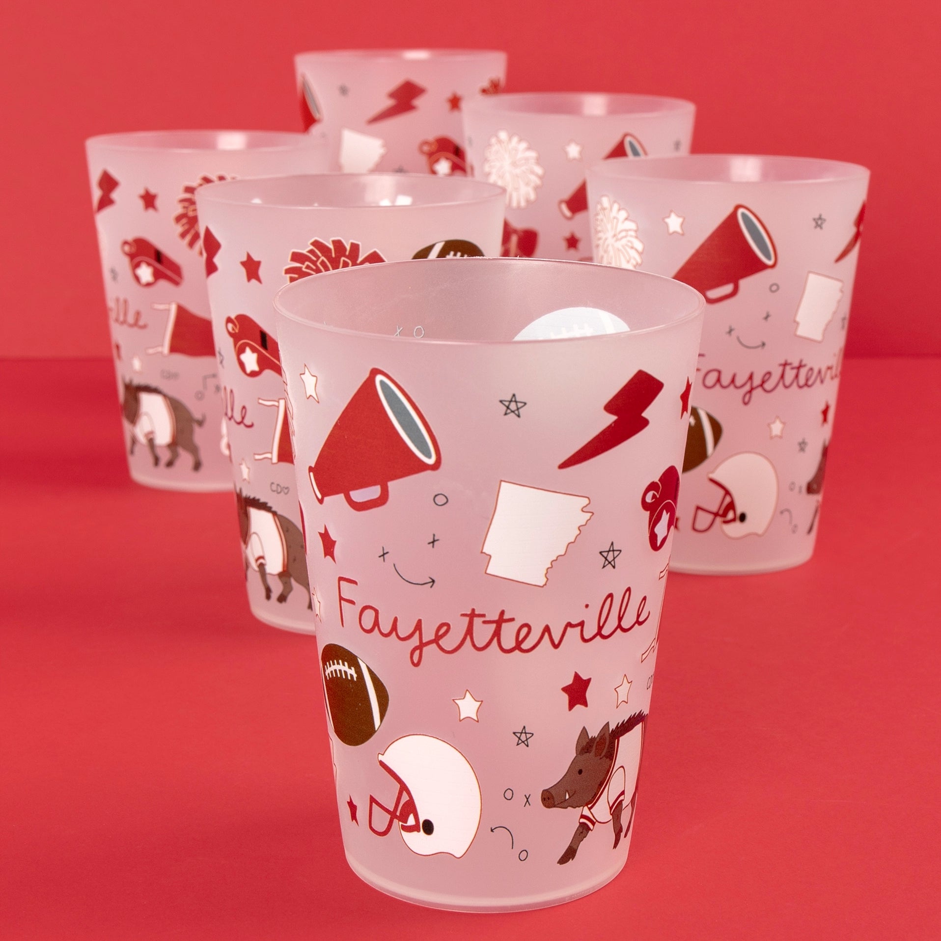 A set of frosted plastic tumblers with red and white Fayetteville football-themed graphics, including a megaphone, football, helmet, and dog, arranged on a solid red background.
