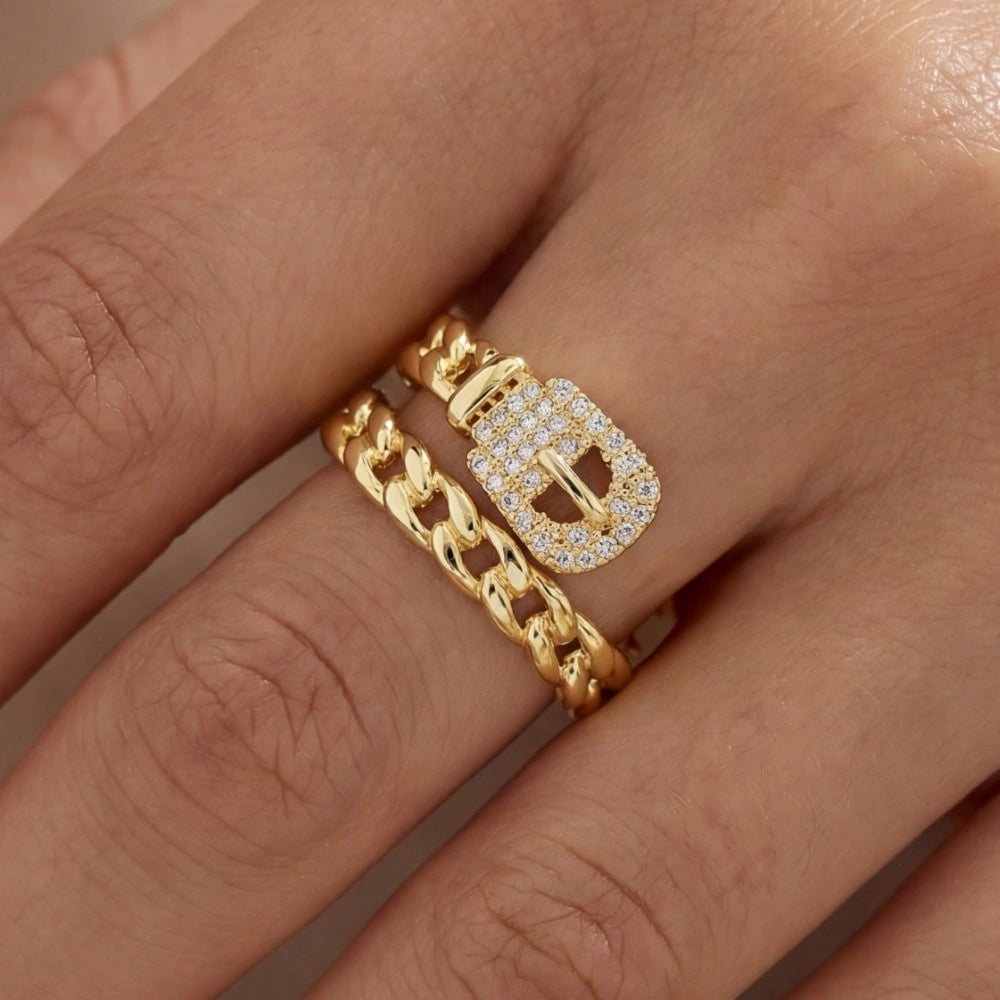 Gold ring with a chain design and buckle detail on a hand.