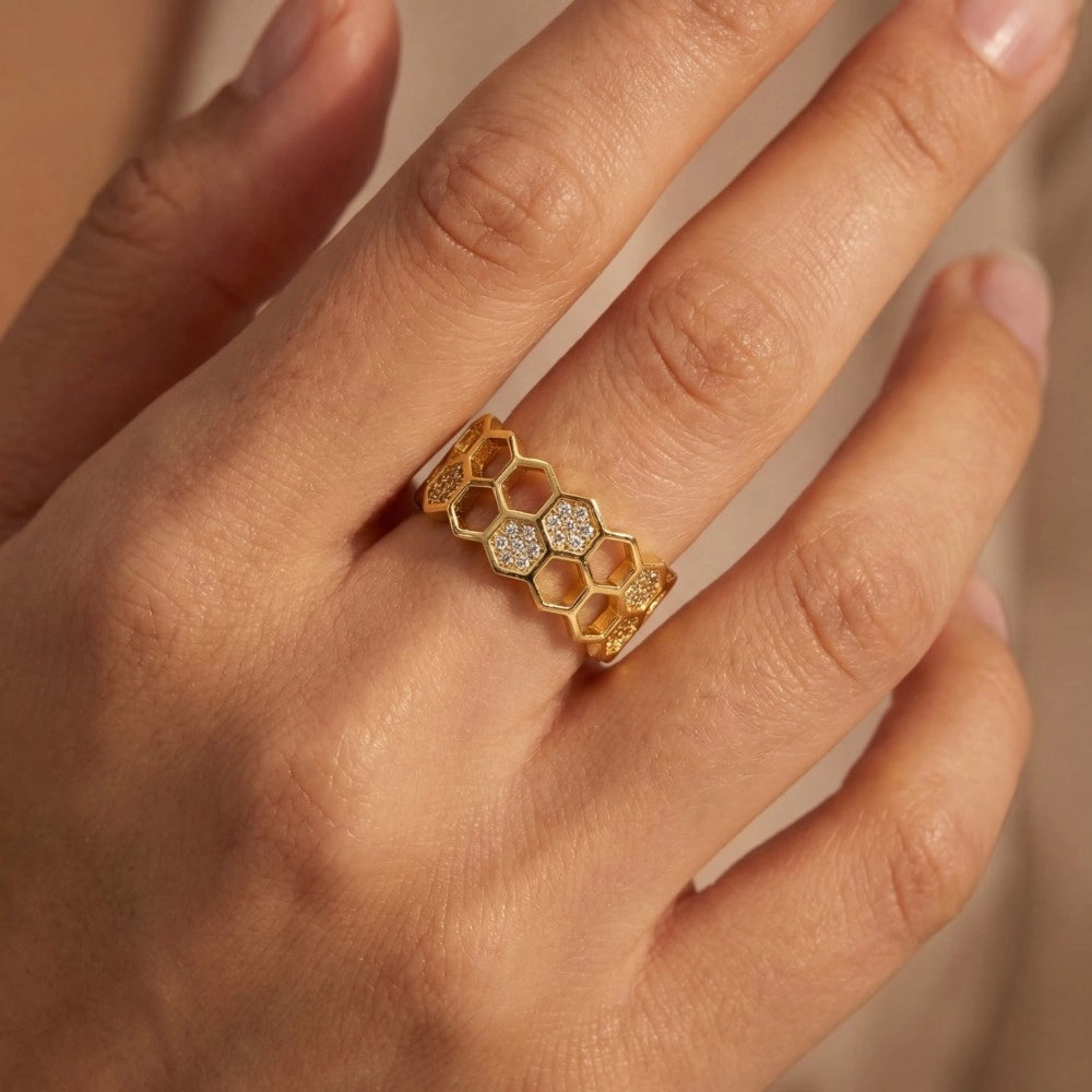 Gold honeycomb ring with embedded diamonds on a hand against a neutral background