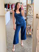 A woman takes a mirror selfie in a boutique wearing a matching blue patterned two-piece set consisting of a sleeveless peplum top and wide-leg cropped pants.