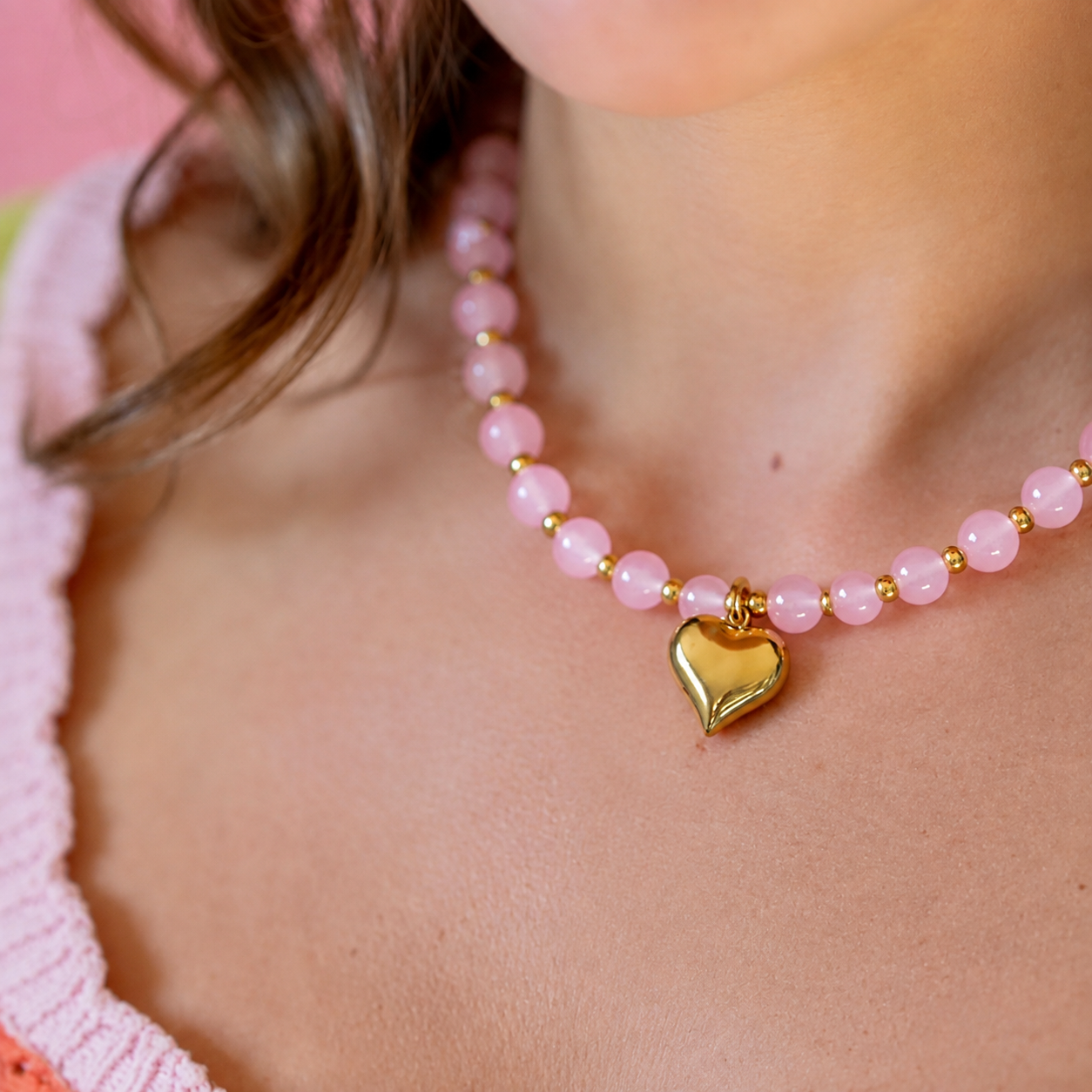 A close-up of a person wearing a pink beaded necklace with a shiny gold heart-shaped pendant.