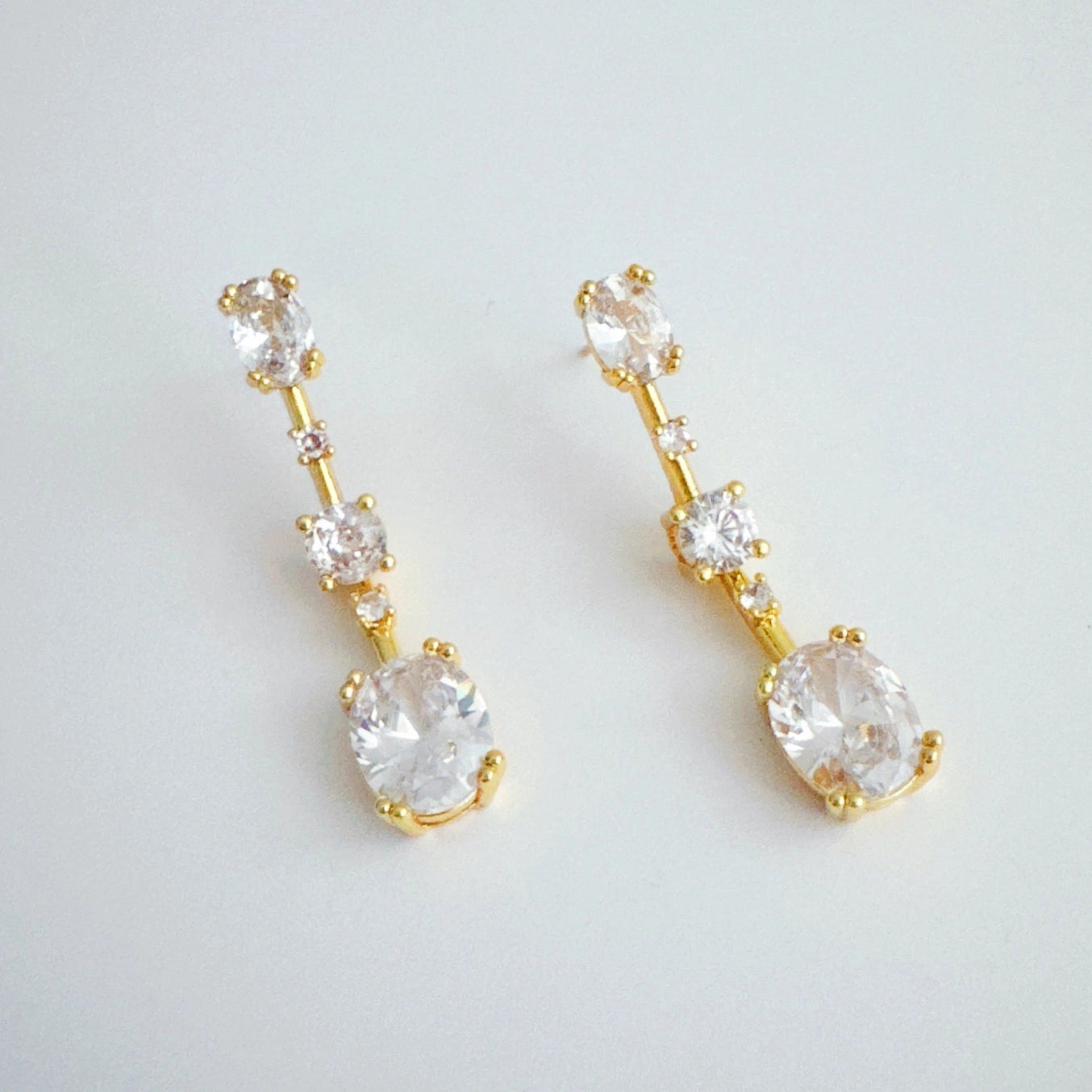 Gold earrings with clear gemstones on a light gray background