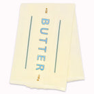 A stack of cream-colored butter wrappers with 'BUTTER' printed vertically in blue letters, flanked by two teal lines, on a plain white background.
