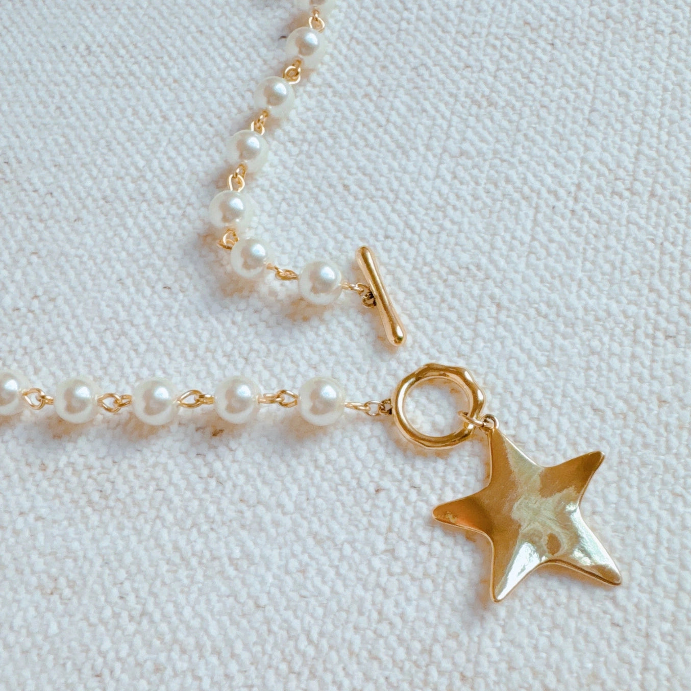 Pearl necklace with a gold star pendant on a light fabric background