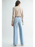 A woman shown from the back wearing a beige long-sleeve cropped sweater and light blue wide-leg jeans against a plain light gray studio background.