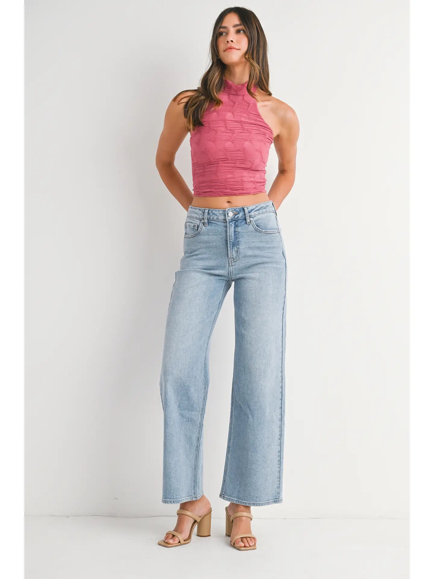 Woman wearing a pink sleeveless top and light blue jeans on a white background