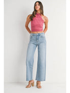 Woman wearing a pink sleeveless top and light blue jeans on a white background