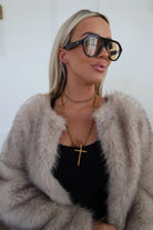 Woman wearing a fur coat, black top, and large sunglasses with a white background