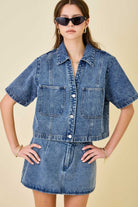 Woman wearing a denim jacket and skirt set with sunglasses on a beige background