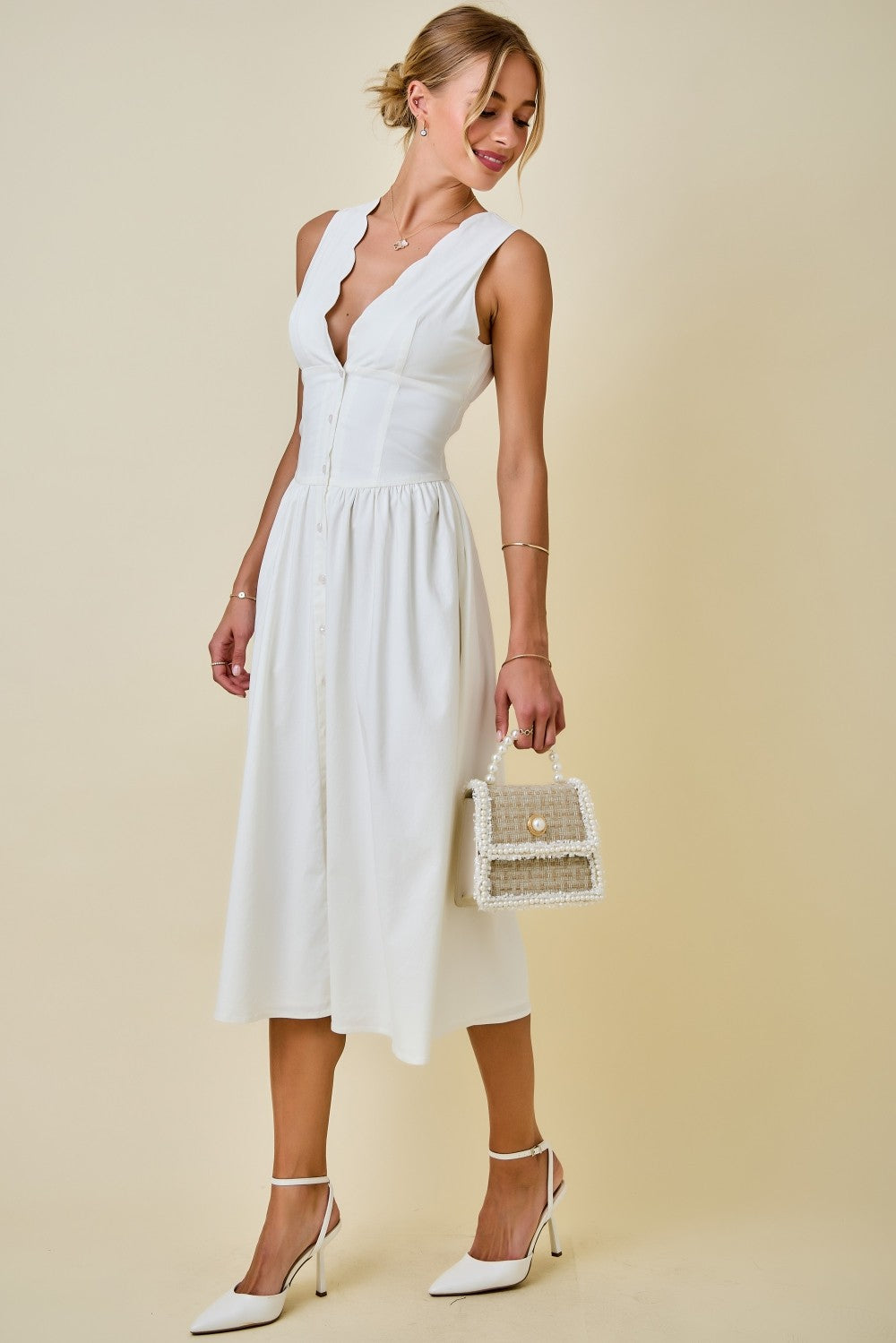 Woman wearing a white dress holding a small bag against a beige background