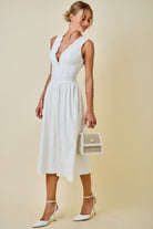 Woman wearing a white dress holding a small bag against a beige background
