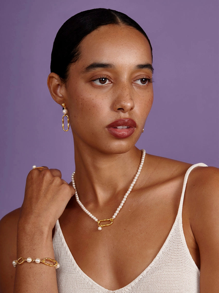 Woman wearing a pearl necklace and earrings against a purple background