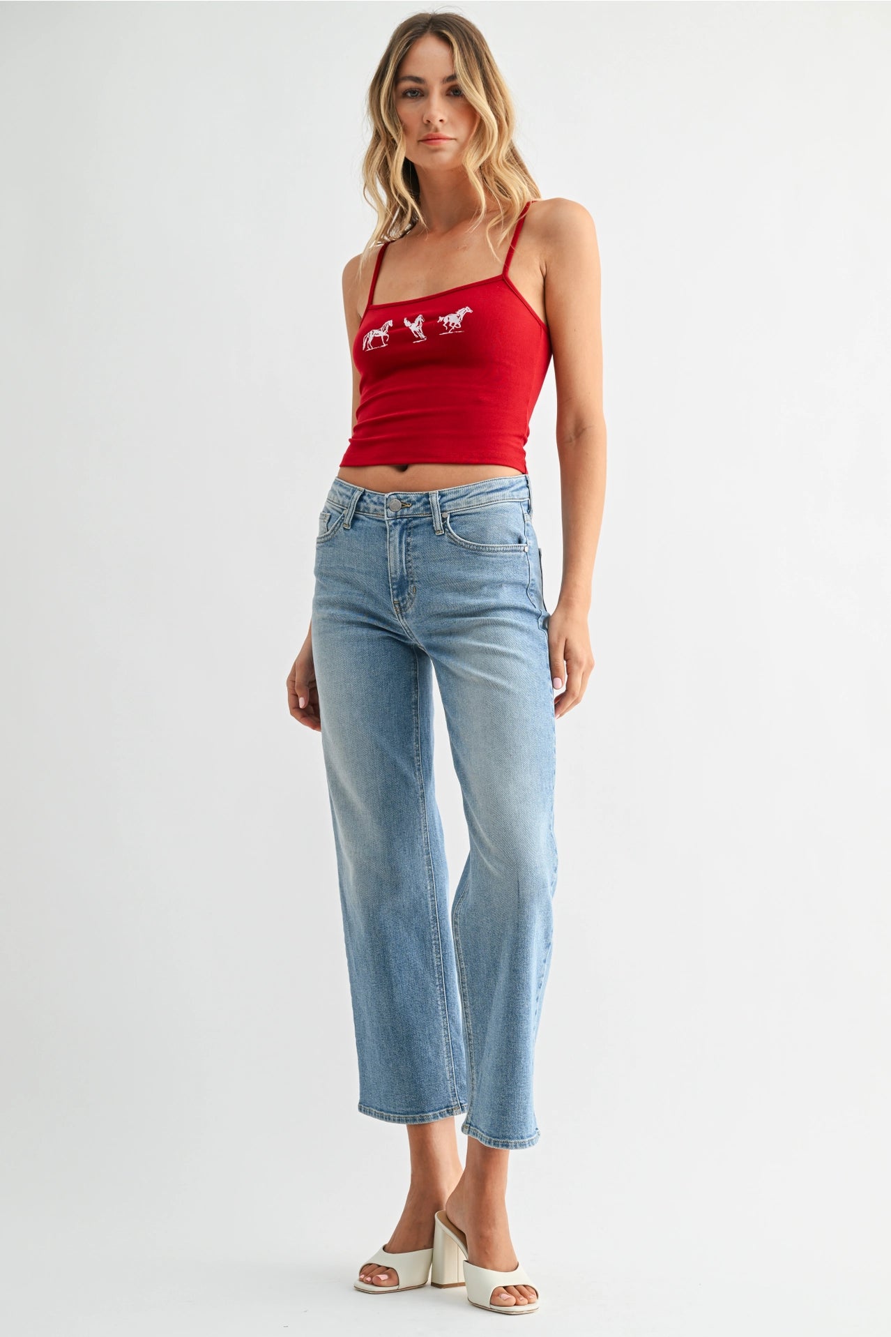 Woman wearing a red tank top with a graphic design and light blue jeans on a white background
