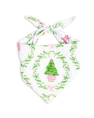 A white pet bandana featuring a festive Christmas print with a green tree in a pink pot, surrounded by a green wreath pattern and pink bows, tied at the top.