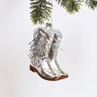 Silver cowboy boot ornament hanging from a tree branch on a white background