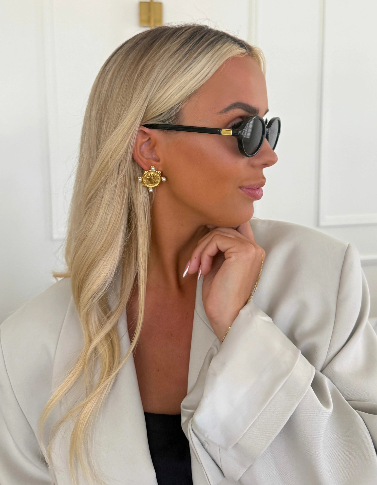 Woman wearing sunglasses and a light-colored coat with a neutral background