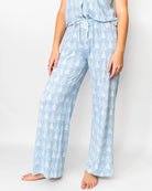 A person wearing light blue pajama pants with a white tree print and a matching top, shown from the waist down against a plain light gray studio background.