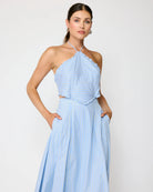 Woman wearing a light blue halter neck dress against a plain background