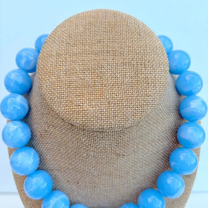 Blue beaded necklace on a tan mannequin head against a light blue background