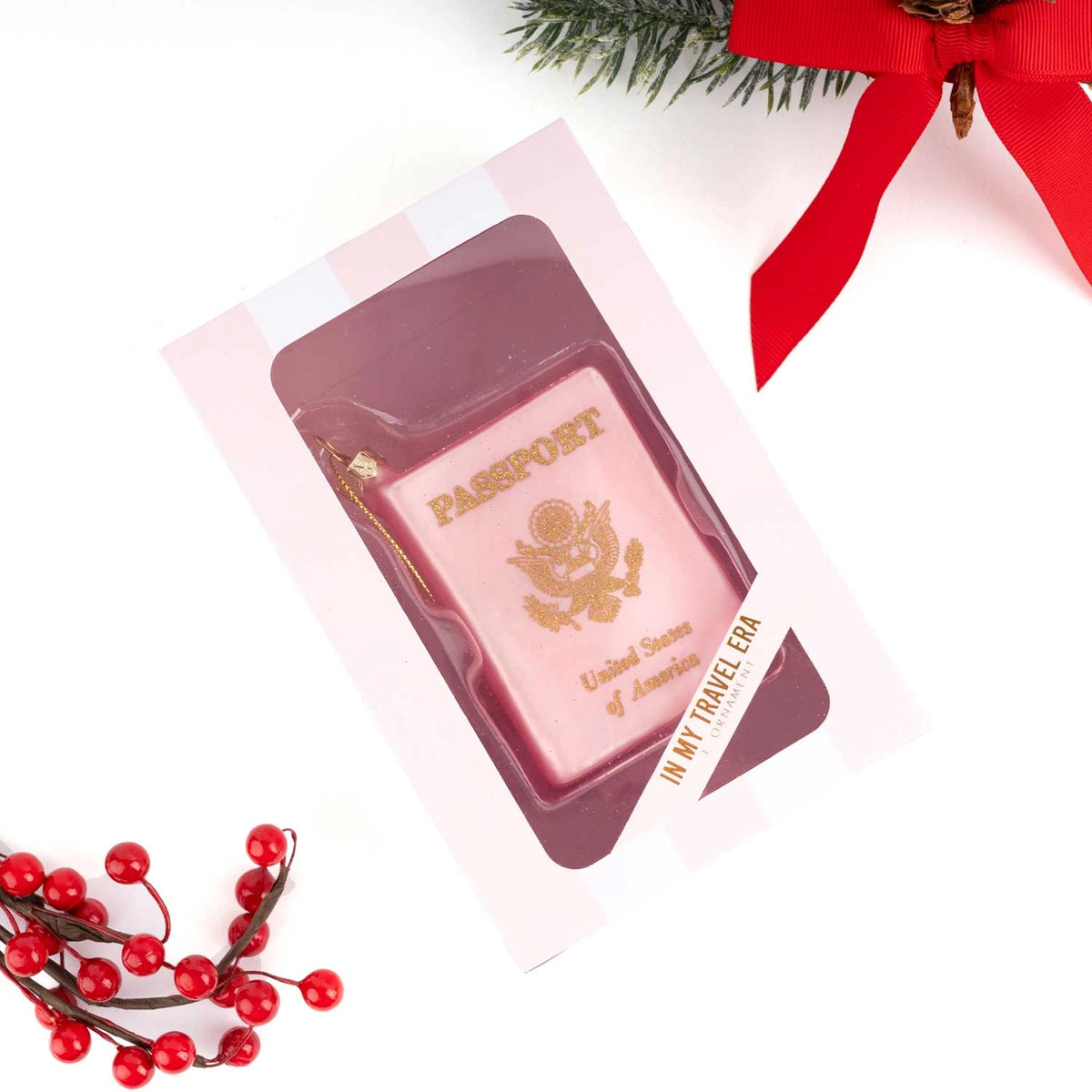 A pink novelty soap bar shaped like a US passport, displayed in a clear windowed pink gift box. The box is photographed on a white background with holiday props, including red berries and a red ribbon.