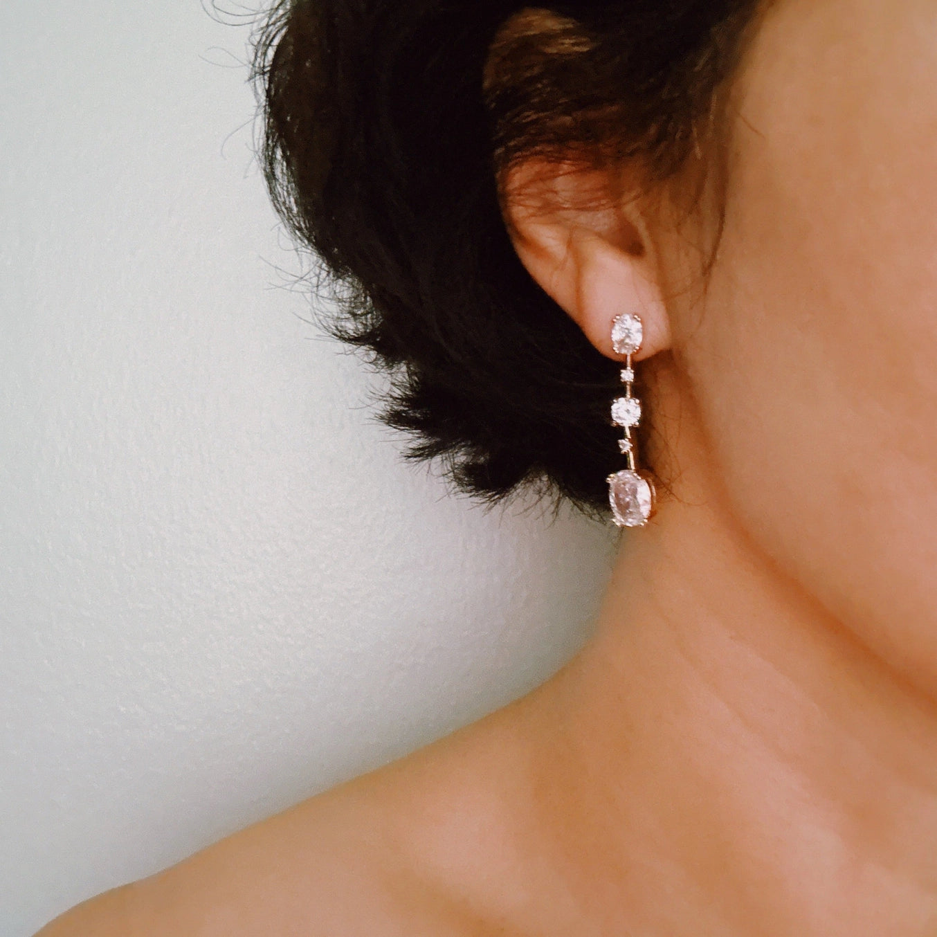 Close-up of an ear wearing a dangling earring with a pink gemstone against a neutral background