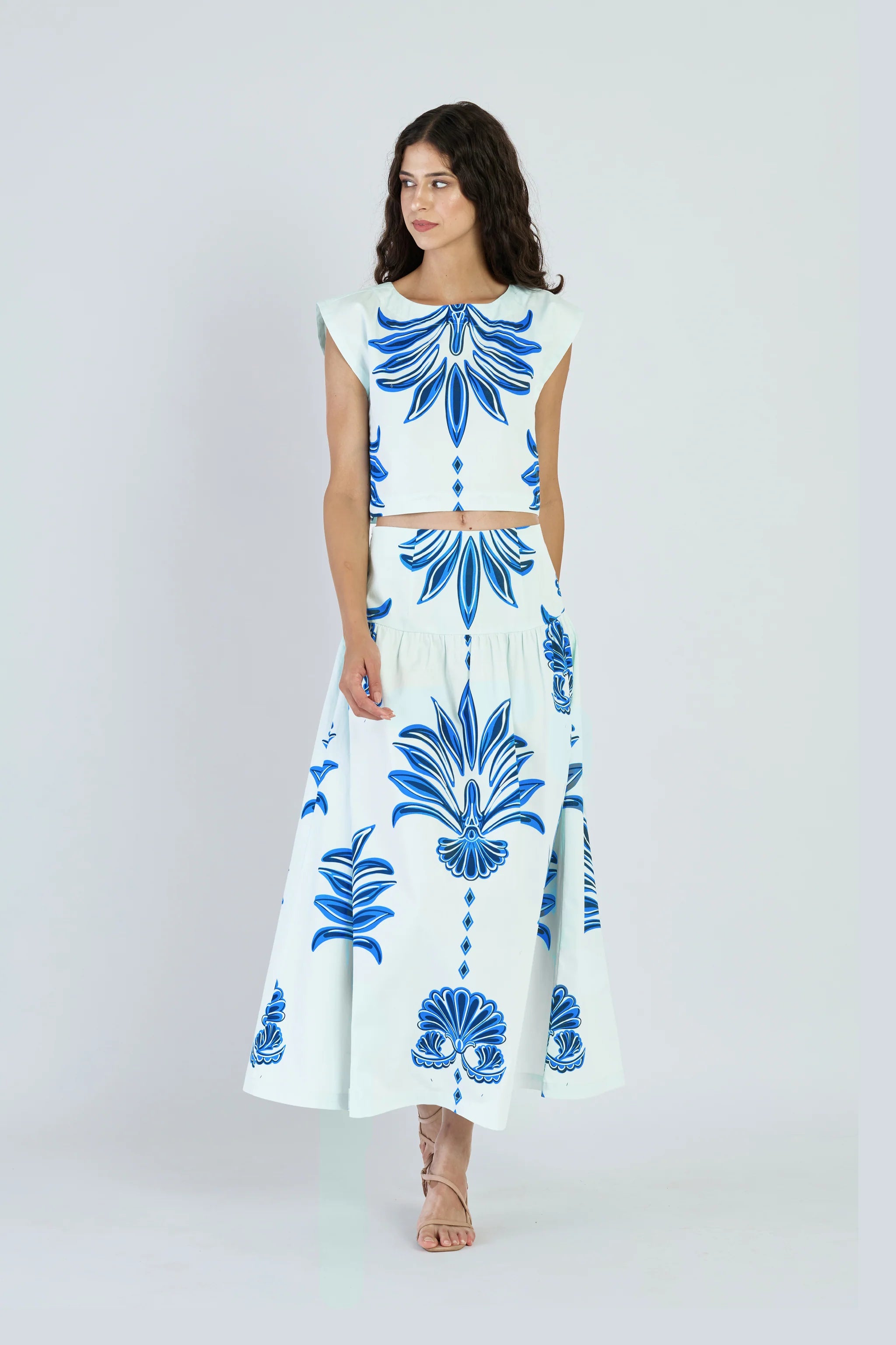 Woman wearing a white outfit with blue floral patterns on a plain background