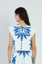 Woman wearing a white dress with blue floral patterns on a plain background