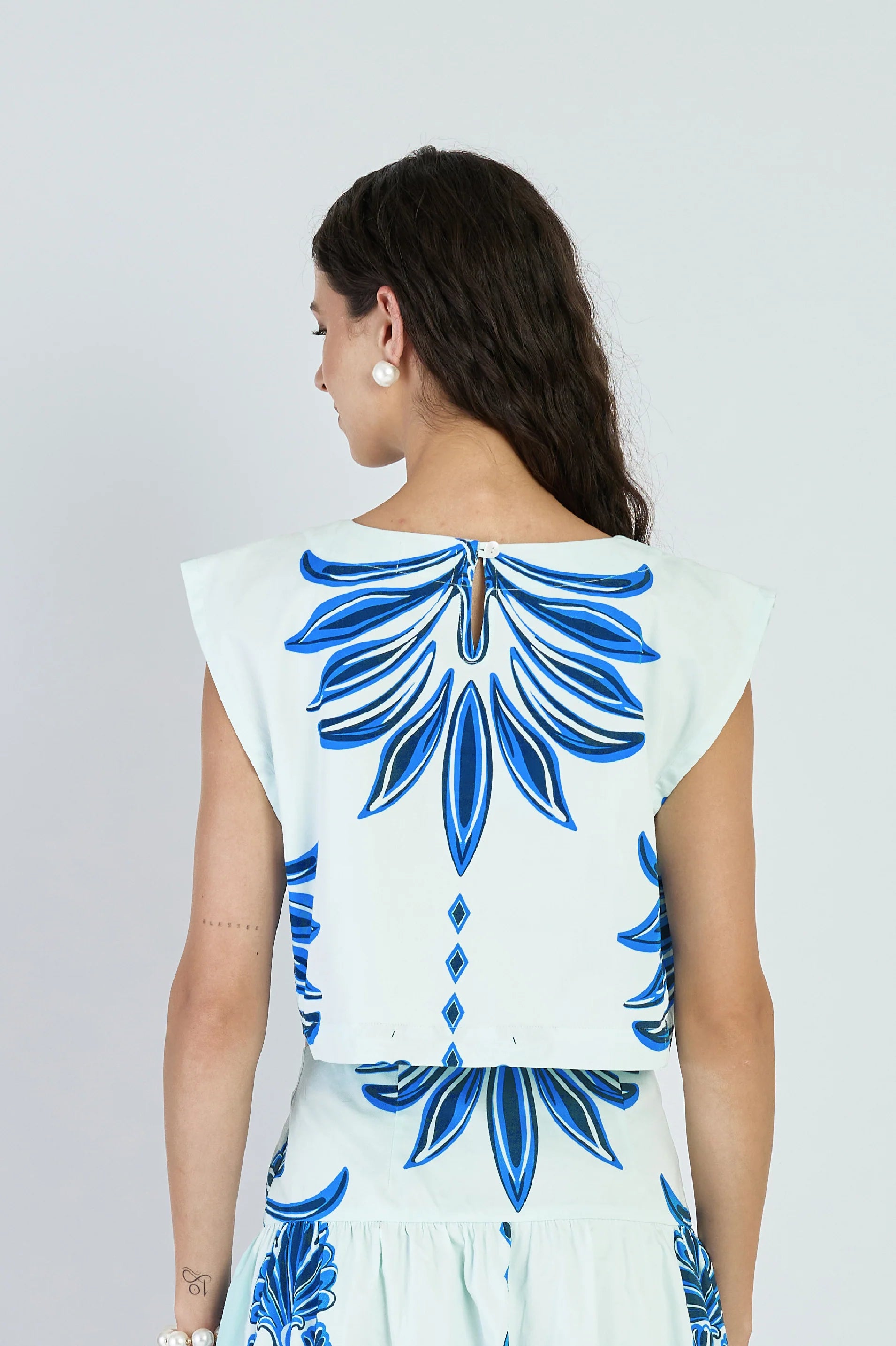 Woman wearing a white dress with blue floral patterns on a plain background