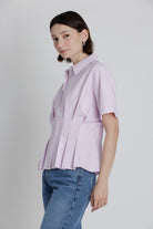 Woman wearing a light pink striped shirt and blue jeans against a plain background