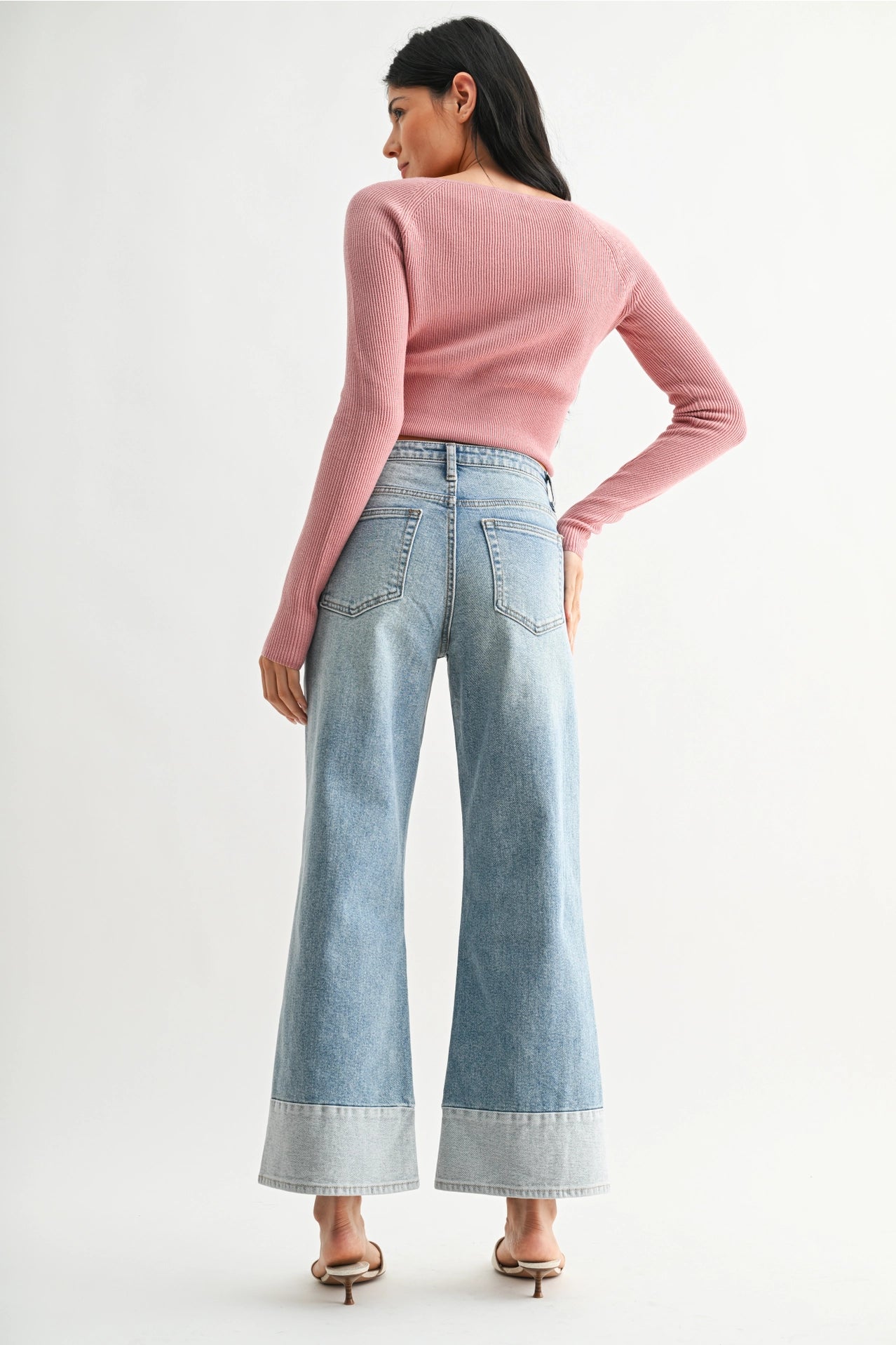 Woman wearing a pink sweater and light blue jeans on a white background