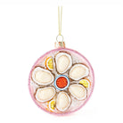 A round glass Christmas ornament styled like a platter of mussels on ice, featuring cream-colored mussel shells, yellow lemon slices, a red-orange center, and a glittery pink rim, hanging by a gold string.