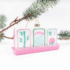 A decorative ornament shaped like three Mahjong-style tiles on a pink glitter base, hanging from a gold loop. The tiles are white with pink, green, and light blue details, including the word "JOKER" on the center tile.