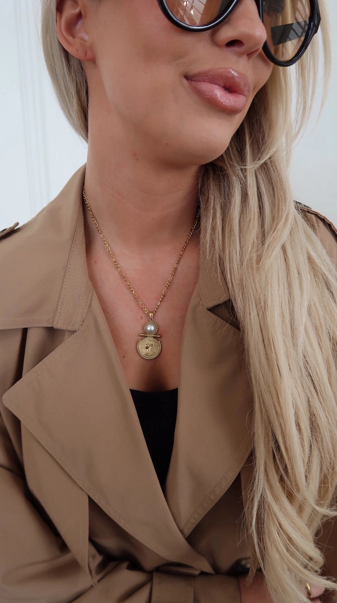 Woman wearing a beige trench coat and sunglasses with a neutral background