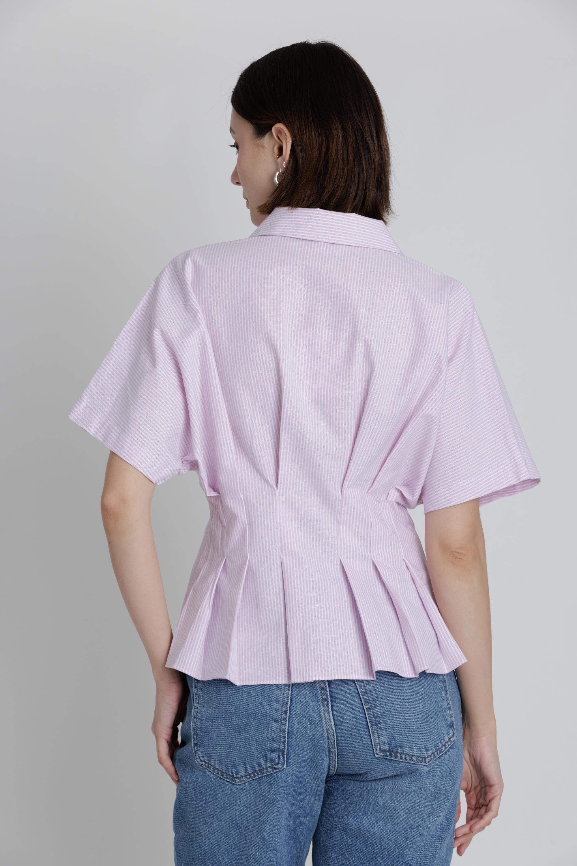 Person wearing a light pink striped peplum shirt and blue jeans on a plain background