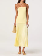 Woman wearing a strapless yellow dress with pleated skirt on a white background