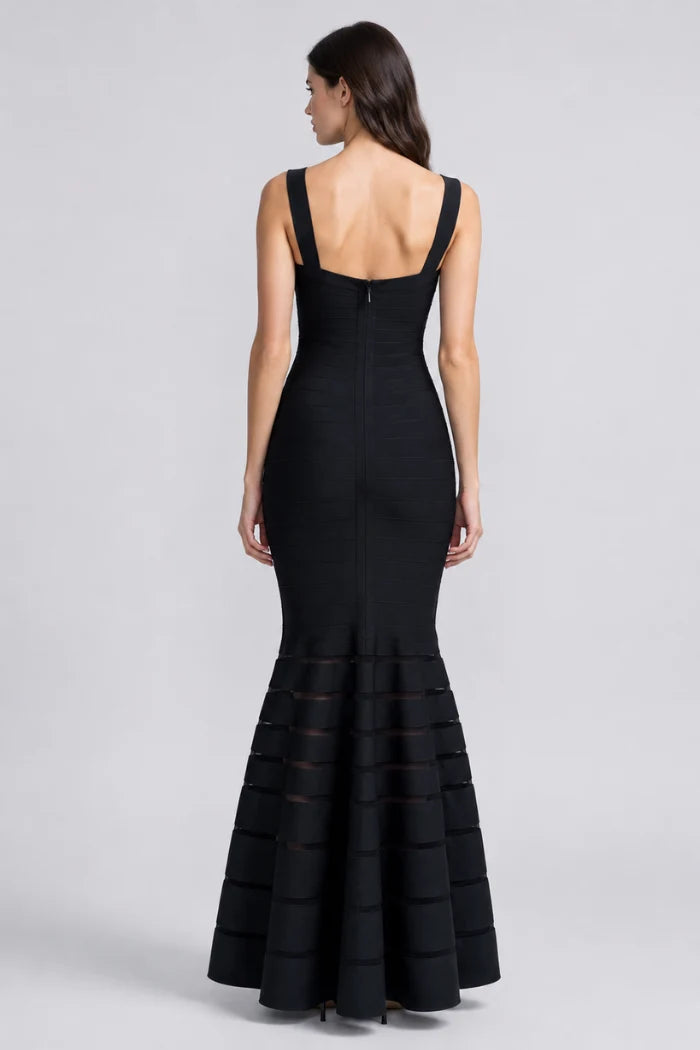 A woman shown from the back wearing a sleeveless black mermaid gown with a structured back and tiered flared skirt, photographed against a light gray studio background.