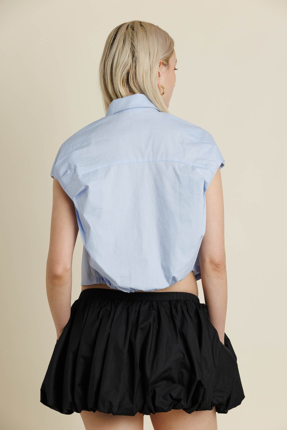 Person wearing a light blue shirt and black skirt on a beige background